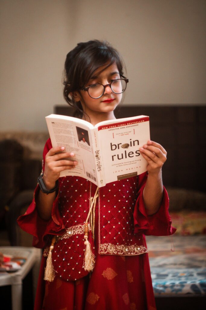 draaya A girl wearing eyeglasses and traditional attire reading 'Brain Rules' indoors.